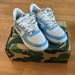 Bapesta Baby blue - Säljer ett par snygga BAPE sneakers i blått och vitt. De har en cool stjärndetalj på sidan och klassisk snörning. Perfekta för att sticka ut i mängden! Skorna är i mycket bra skick och kommer i originalkartong med camouflage-mönster.