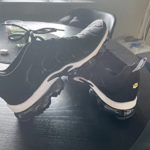 Svarta Nike Air Vapormax - Säljer ett par svarta Nike Air Vapormax i nyskick. De har en snygg och modern design med synlig luftdämpning i sulan för extra komfort. Skorna har snörning och en liten Nike-logga på sidan. Perfekta för vardagsbruk! Kommer ej till användning, därav säljer jag!