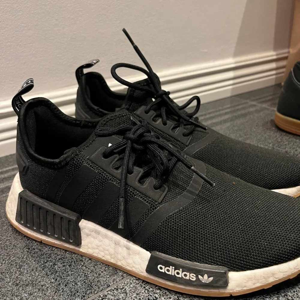 Säljer ett par svarta Adidas NMD sneakers i bra skick. De har en stilren design med vit sula och klassiska tre ränder på sidan. Perfekta för både vardag och träning. Sköna och lätta att matcha med olika outfits!. Skor.