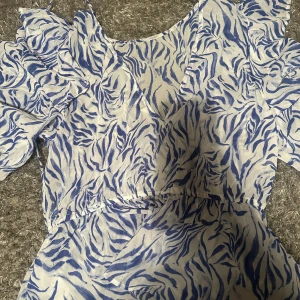 Blåvit Blus med zebramönster från Kappahl - Säljer en aldrig använd superfin blåvit Blus från Kappahl med zebramönster. Den har korta ärmar med volangdetaljer och en smickrande passform. Perfekt för sommardagar eller en festlig kväll. 🦓💙