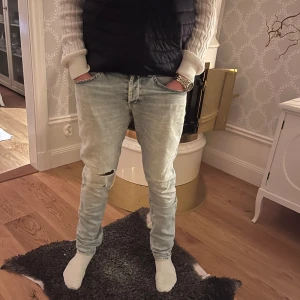 Dondup Jeans - Säljer ett par ljusa Dondup Jenas i bra skick med slitningar på knäna. De har modellen George och är slim fit, och är perfekta för en avslappnad stil. Jeansen har en klassisk femficksdesign och är tillverkade i bomull. Perfekta för både vår och höst!