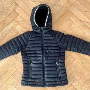Svart dunjacka från Peak Performance - Säljer en svart dunjacka från Peak Performance i mycket bra skick. Jackan har en snygg quiltad design med dragkedja och huva. Perfekt för höst och vinter, håller dig varm och stilren. Passar både till vardags och utomhusaktiviteter.Längd 59cm, bred 46cm. Har avtagbar luva och justerbar midja. 