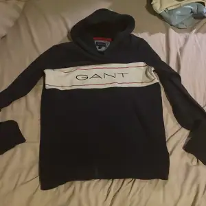 Säljer en snygg mörkblå hoodie från GANT i storlek S. Den har en vit och röd rand över bröstet med GANT-loggan. Perfekt för en avslappnad stil och passar bra till jeans. 