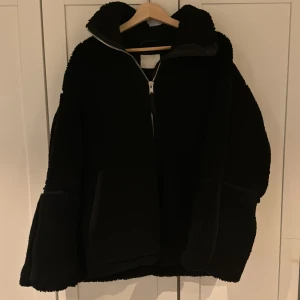Svart teddyjacka från H&M - Mysig svart viral  teddyjacka från H&M i storlek M. Perfekt för kyliga höst- och vinterdagar. Jackan har en dragkedja framtill och är långärmad med en skön, oversized passform. Den är i mycket bra skick och redo att hålla dig varm och stilren. 🖤