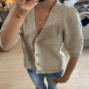Beige stickad kofta - Säljer en superfin beige stickad kofta med knappar framtill. Den har en v-ringad design och trekvartsärmar, perfekt för både vår och höst. Koftan är i bra skick och passar till både jeans och kjol. Perfekt för en mysig dag ute eller hemma! 💫