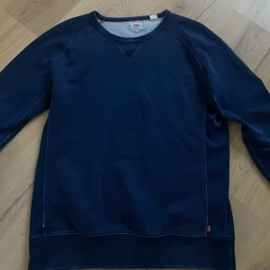 Mörkblå tröja från Levi's - Säljer en snygg mörkblå tröja från Levi's i storlek M. Tröjan har en klassisk design med rund hals och långa ärmar. Perfekt för en avslappnad stil och passar bra till både jeans och chinos. Den är i bra skick och redo för en ny ägare!