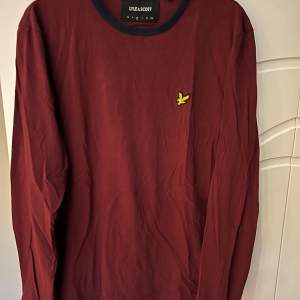 Säljer en snygg vinröd långärmad t-shirt från Lyle & Scott med deras ikoniska logga på bröstet. Tröjan har långa ärmar och en klassisk rund halsringning. Perfekt för både vardag och lite finare tillfällen. Passar bra till höst och vinter!Storlek medium. 