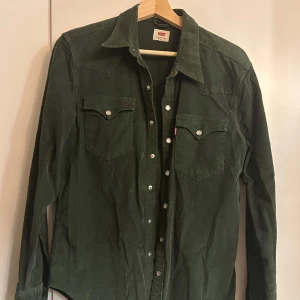 Grön manchester skjorta från Levi's XS/S - Säljer en snygg grön manchester skjorta från Levi's. Skjortan har långa ärmar och knappar framtill samt på bröstfickorna. Perfekt för höst och vinter, med en skön och stilren look. Passar både till vardags och lite mer uppklädda tillfällen. Skjortan är i storlek S, men skulle säga att den är liten i storleken och passar XS/S
