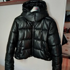 Svart pufferjacka från NA-KD - Säljer en snygg svart pufferjacka från NA-KD i storlek 36. Jackan är i mycket bra skick och perfekt för höst och vinter. Den har en dragkedja framtill och en hög krage samt luva för extra värme. Perfekt för att hålla stilen när det är kallt ute! 🖤