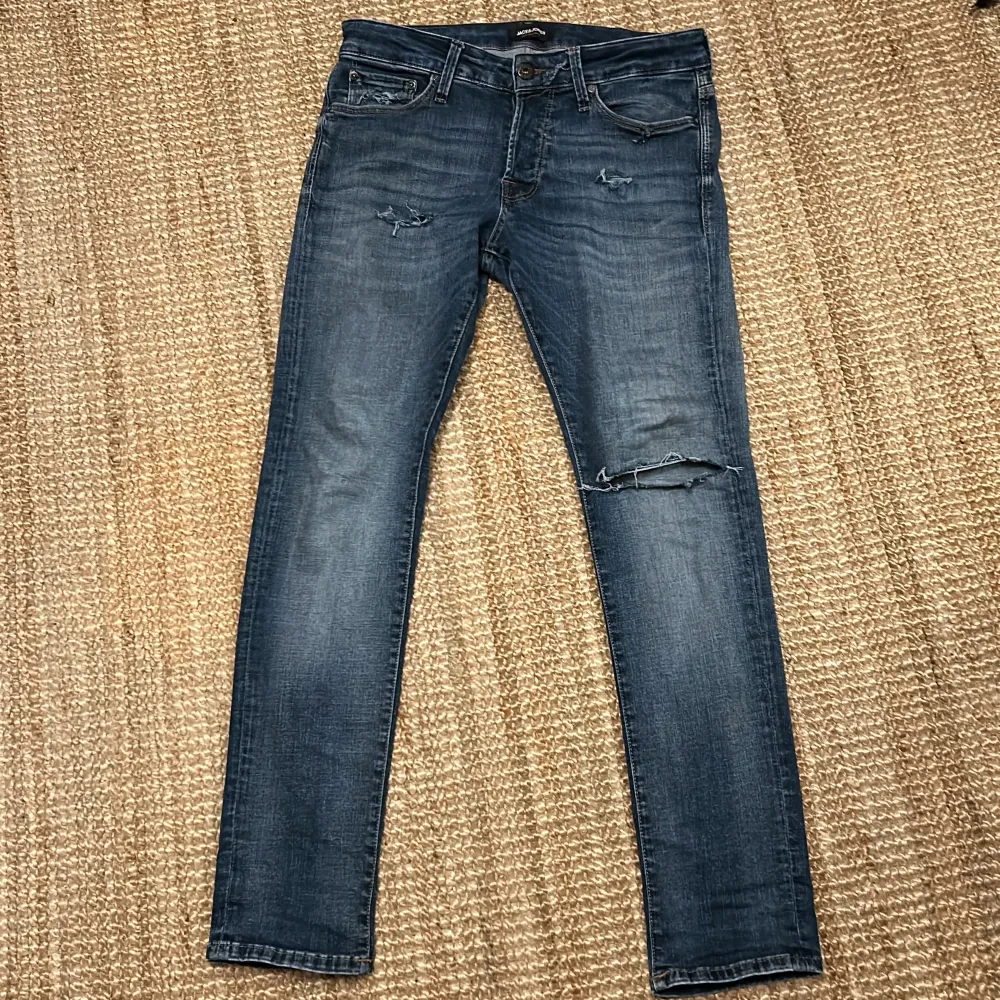 Säljer ett par snygga blå jeans i slim fit med slitningar på knäna och fickorna. Perfekta för en casual look! De har en klassisk femficksdesign och är i bra skick. Passar både till vardags och fest.. Jeans & Byxor.