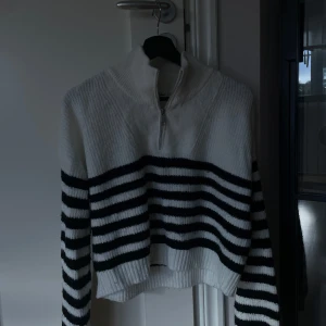 Vit och svart randig stickad tröja - Säljer en supermysig vit och svart randig stickad tröja med dragkedja i halsen. Perfekt för kyliga dagar och ger en stilren look. Tröjan har långa ärmar och en bekväm passform. Passar perfekt till både jeans och kjol!