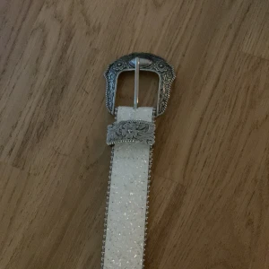 Glittrigt vitt bälte med silverdetaljer - Säljer ett glittrigt vitt bälte med snygga silverdetaljer, ca 100cm långt och passar med de flesta byxorna. Jag har inte haft de så länge o inte använt så jätte mycket heller, vilket är anledningen till att jag säljer de💞