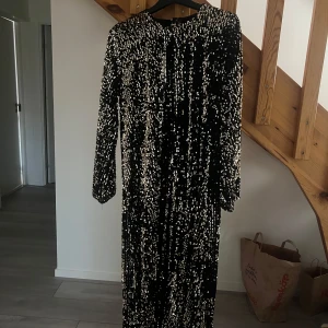 Svart glittrig långklänning - Säljer en superglittrig svart långklänning med paljetter över hela tyget. Perfekt för nyårsfesten eller en glamorös kväll ute. Klänningen har långa ärmar och en elegant passform som verkligen fångar ljuset. Ett måste för den som vill sticka ut!
