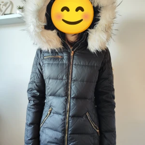 Svart dunjacka från Rockandblue - Säljer en snygg svart dunjacka från Rockandblue i storlek 36. Jackan har en fluffig pälsfodrad huva och dragkedja framtill. Perfekt för kalla vinterdagar med sin quiltade design och långa ärmar. Den har praktiska fickor med dragkedjor för säker förvaring. Håll dig varm och stilren i vinter! ❄️