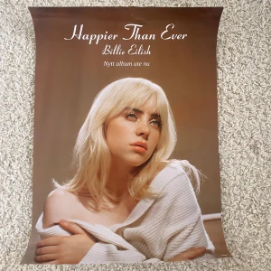 Billie Eilish poster - En affisch för albumet 'Happier Than Ever' av Billie Eilish. Den visar en bild av artisten med blont hår och en vit tröja. Perfekt för fans som vill dekorera sitt rum med något stilrent och aktuellt. Den är oanvänd men köpt second hand. Skriv gärna vid frågor.
