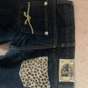 Säljer ett par mörkblå jeans med coola leopardmönstrade fickdetaljer och glittriga knappar. De har en tight passform och låg midja. De är äckta just cavalli. Storleken på lappen är 27. Midjemåttet är 37cm. Innerbenslängden är 72cm. Observera att hela jeansen är glittriga. Kan sänka priset vid snabbt köp! 