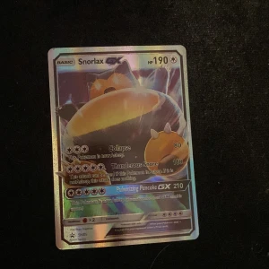 Snorlax GX Pokémonkort - Säljer ett Snorlax GX Pokémonkort med 190 HP. Kortet har en holografisk yta som ger en cool regnbågseffekt. Det har attacker som 'Collapse' och 'Thunderous Snore', samt en speciell GX-attack 'Pulverizing Pancake'. Perfekt för samlare eller Pokémon TCG-spelare!
