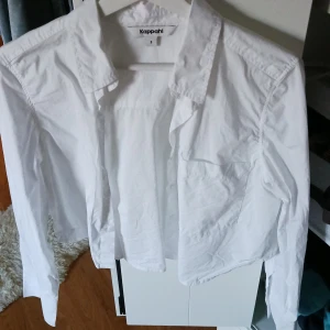 Vit skjorta från Kappahl - Säljer en kropped vit skjorta från Kappahl i storlek S. Skjortan har långa ärmar och är perfekt för både vardag och fest. Den är i bra skick och gjord av bomull, vilket gör den bekväm och lätt att bära. Passar perfekt till jeans eller en snygg kjol!