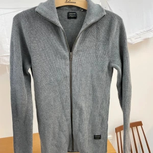 Grå stickad kofta Jack and Jones - Säljer en stilren grå stickad kofta från Jack & Jones. Fullzip, perfekt att ha tex över en Skjorta. Perfekt för höst och vinter! Storlek M, skriv PM vid minsta fråga. BVSA
