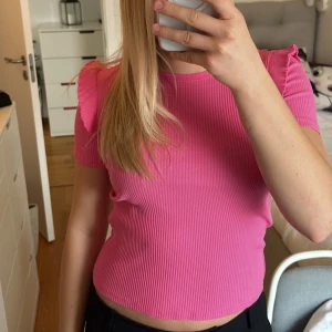 Rosa ribbad topp från Zara - Säljer en superfin rosa ribbad topp med liten volang på axlarna från Zara. Toppen har tight passform och är i mycket bra skick. Perfekt för både vardag och fest! 💖köparen står för frakten💖