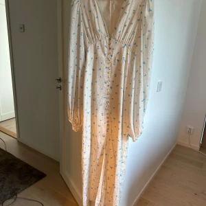 Vit långklänning med blommönster - Säljer en superfin vit långklänning med små blå blommor. Den har en v-ringad design och knappar framtill. Ärmarna är långa och klänningen har en romantisk stil, perfekt för vår och sommar. Passar både till fest och vardag! Slutsåld på ADOORE .Använd endast en gång varsamt därmed inga defekter 🤍🩵