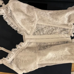 Vit spetskorsett - Säljer en superfin vit korsett i spets. Den har justerbara axelband och en vacker blommig spetsdesign. Perfekt för en fest eller speciellt tillfälle. Den är i mycket bra skick och ger en elegant look.