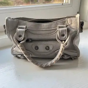 Säljer en snygg grå handväska i skinn med coola detaljer. Väskan har en dragkedja framtill och fins handtag. Perfekt för både vardag och fest! 👜efterliknar en väska från ett känt och dyrt märke. 