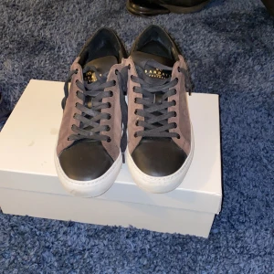 Bruna och svarta mocka sneakers från Sandays - Snygga sneakers från Sanday i brunt mocka med svarta detaljer och snörning. De har en vit sula som ger en fräsch look. Perfekta för både vardag och festliga tillfällen. Skorna är i exremt bra skicik, nästan ny skick, vid funderingar eller frågor skriv privat, PRISET ÄR ABSOLUT INTE HUGGET I STEN OCH GÅR ATT DISKTUTERA ÄR OCKSÅ ÖPPEN FÖR BYTEN!