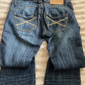 Blå jeans från Base Jeans - Säljer ett par snygga blå jeans från Base Jeans i mycket bra skick. De har en klassisk femficksdesign med coola kontrastsömmar och en knappgylf.  Lågmidjade och utsvänga 