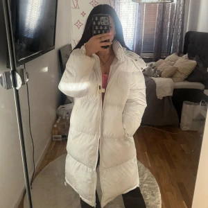 Vit lång pufferjacka - Säljer en supermysig vit pufferjacka som är perfekt för vintern. Den är köpt från pretty little thing för något år sedan men har inte använt den så ofta då jag har andra jackor. Den är lång (jag är 164cm) och har en stor huva som skyddar mot kylan. Jackan har en dragkedja framtill och är i mycket bra skick. Den har även två fickor. Perfekt för kalla dagar när du vill hålla dig varm och snygg.