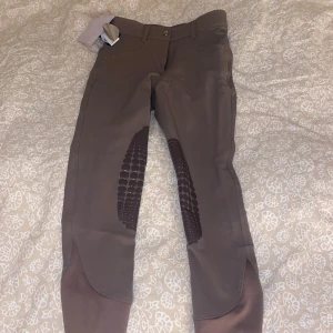 Beiga ridbyxor från CRW - Säljer ett par snygga bruna ridbyxor från CRW i storlek 34.Förstärkningar på insidan av benen för extra grepp. Byxorna är helt oanvända med lappen kvar och extra stenar därav pris kan dock diskuteras. Nypris 999sek. Färgen är något mer beige i verkligheten. 