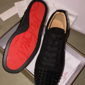 Säljer ett par svarta sneakers från Christian Louboutin i nytt skick storlek 42. Skorna har en cool design med svarta nitar på tån och den ikoniska röda sulan. Perfekta för att ge din outfit en edgy touch! Kommer med lförpackning och papper och extra spikar. Kan mötas upp 