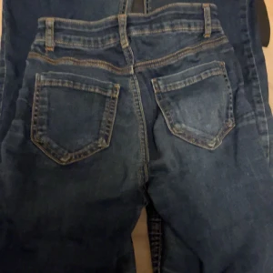 Blå jeans i bra skick - Säljer ett par blå jeans i bra skick. De har en klassisk design med fem fickor och en dragkedja. Det finns ett litet slitage på ena benet, men det ger dem bara lite extra karaktär. Perfekta för vardagsbruk! 