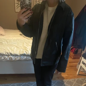 Svart skinnjacka - Säljer en snygg svart skinnjacka i bra skick. Den har en klassisk stil med dragkedja framtill och två fickor med dragkedjor. Perfekt för höst och vår, och funkar både till vardags och fest. Jackan har en normal passform och långa ärmar. Använd endast 2 gånger!! Nypris: 699