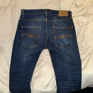 Nudie Jeans Grim Tim - Säljer ett par snygga blå jeans från Nudie i bra skick. De har en klassisk femficksdesign med orange sömmar och en knappgylf. Perfekta för både vardag och fest! 🕺Modellen är Grim Tim i storlek 31/32. Sparsamt använd med inga defekter! Hör av er om ni har några frågor! 