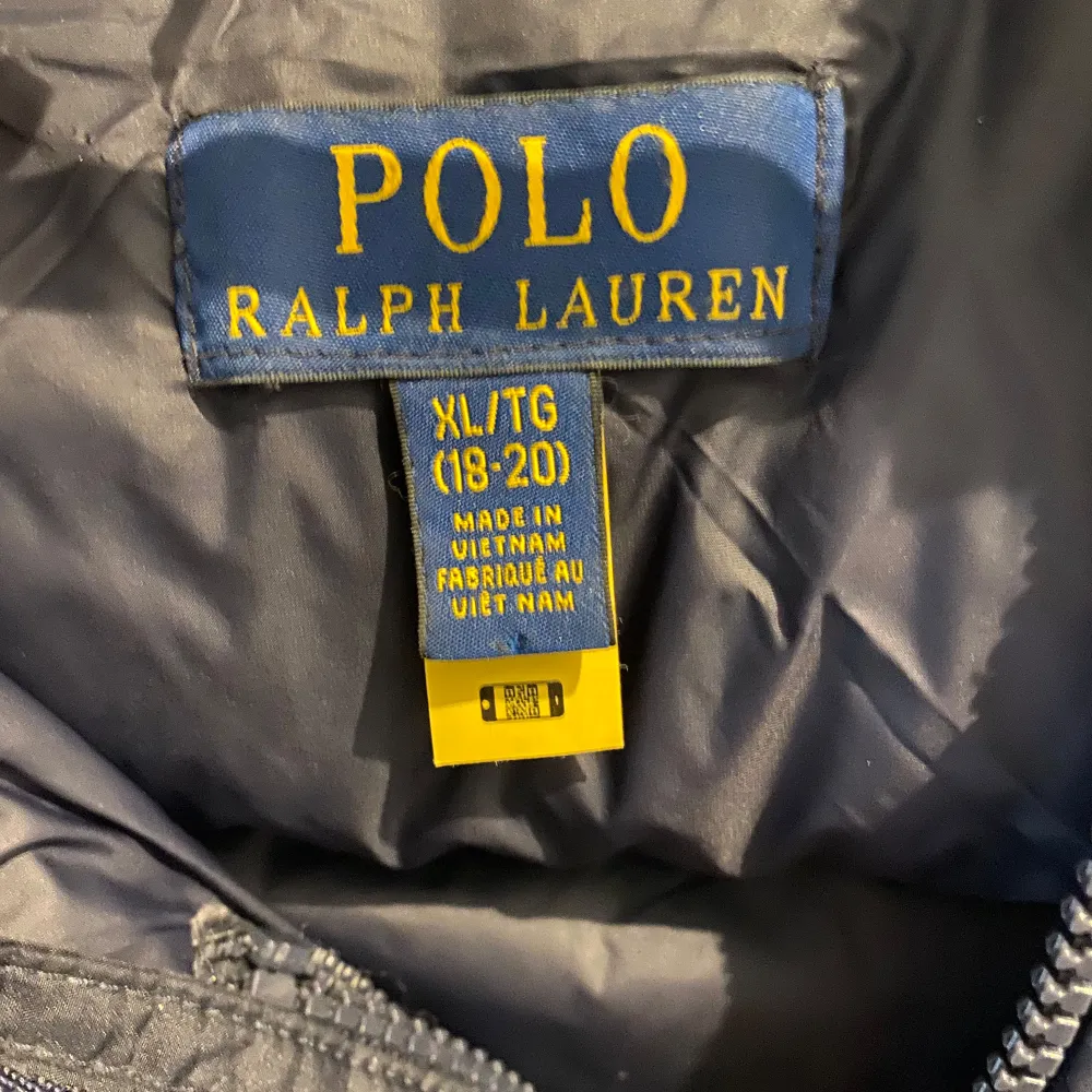 Säljer en snygg marinblå dunjacka från Polo Ralph Lauren i storlek XL barn. Jackan har en dragkedja framtill och två praktiska fickor med dragkedjor. Den är perfekt för kalla vinterdagar och har en klassisk design med det ikoniska logotypen broderad i rött på bröstet. Huvan är avtagbar för extra flexibilitet.. Jackor.