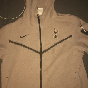 Grå huvtröja från Nike med Tottenham Hotspur-logga - Säljer en grå huvtröja från Nike med Tottenham Hotspur-logga på bröstet. Tröjan har en dragkedja framtill och är perfekt för höst och vår. Den är i bra skick och passar både till vardags och träning. Perfekt för alla Spurs-fans! 💙