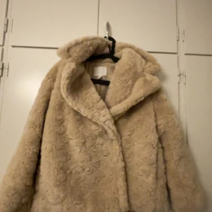 Beige päls jacka  - Mysig beige pålsjacka i mycket bra skick. Inte använd. Passar en S och en M. Perfekt för kalla vinterdagar. Jackan har en oversized passform och långa ärmar, vilket gör den superbekväm och trendig. Den är gjord av mjukt syntetmaterial som håller dig varm och stilren.