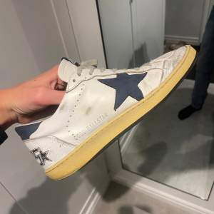 Säljer ett par Golden Goose sneakers i vitt med en cool blå stjärna på sidan. Skorna har en vintage-look med gul sula och texten 'SNEAKERS' på hälen. Perfekta för en avslappnad stil med en touch av lyx. De är i bra skick med lite slitage som ger dem karaktär Skorna är i storlek 41 men passar mig som vanligtvis har 42. Hör av er vid fler frågor eller funderingar 