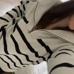 Randig stickad tröja med dragkedja - Säljer en supermysig stickad tröja med dragkedja i kragen. Den är vit med svarta ränder och har långa ärmar. Perfekt för höst och vinter när du vill hålla dig varm och stilren. 