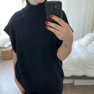 Svart stickad polotröja - Säljer en svart stickad poloväst, oanvänd med lapp kvar. Den har en hög krage och är ärmlös. Västen är oversized. 