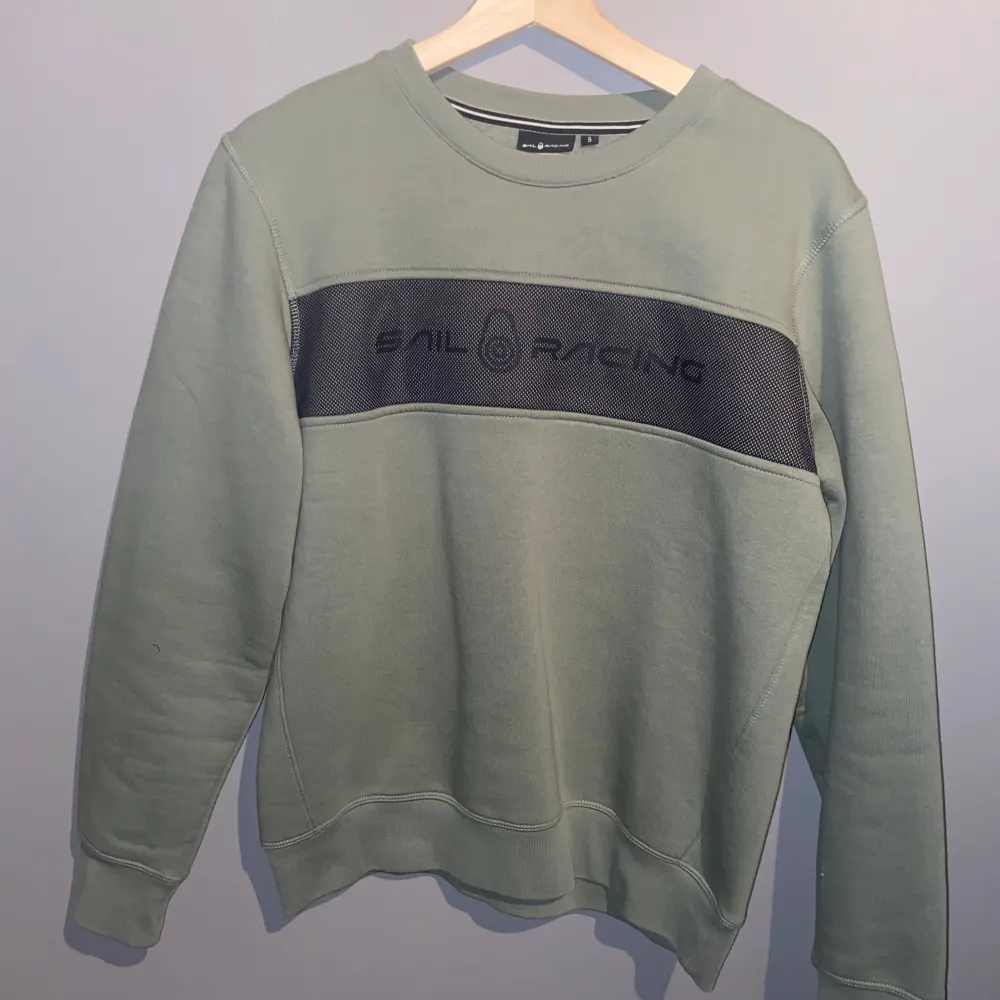 Säljer en snygg grön sweatshirt från Sail Racing i storlek S. Tröjan har en svart panel med logotypen på bröstet och är perfekt för en avslappnad stil. Den är i mycket bra skick och passar perfekt för höst och vår.. Hoodies.