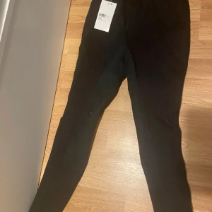 Svarta ridbyxor - Säljer ett par svarta ridbyxor i storlek 164. De är tillverkade av 96% bomull och 4% spandex, vilket gör dem både bekväma och stretchiga. Perfekta för ridning och har en tight passform. Byxorna är i nytt skick med etikett kvar.