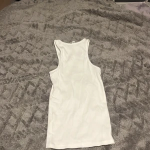 Vit ärmlös topp från H&M - Säljer en snygg vit ärmlös topp från H&M i storlek XS. Perfekt för sommardagar eller som ett basplagg i garderoben. Toppen är i nytt skick och har en ribbad struktur som ger en stilren look. Passar både till vardags och festliga tillfällen! Vet att pris lappen är oanvändbar, men fick den i present.🩷Har Aldrig använts! 