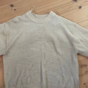 Beige stickad tröja från H&M - Mysig vit stickad tröja från H&M i storlek XS. Perfekt för kyliga dagar med sin mjuka och varma känsla. Tröjan har en klassisk rund hals och ribbade muddar vid ärmslut och nederkant. Passar både till vardags och mysiga hemmakvällar.