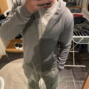 Säljer en stilren grå hoodie från Smog i storlek M. Den har en dragkedja framtill och är i slim fit, perfekt för en casual look. Materialet är mjukt och bekvämt, idealiskt för både höst och vår. Sitter litet för M då den är en slim men perfekt som S