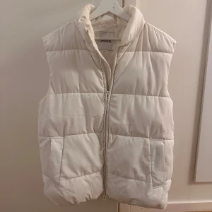 Vit dunväst från Monki - Säljer en snygg vit dunväst från Monki i storlek S. Västen har en dragkedja framtill och är quiltad för extra värme. Den är i bra skick men med små fläckar och skav på dragkedjan.