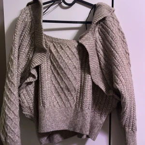 Beige stickad tröja med volangdetaljer - Säljer en superfin beige stickad tröja med volangdetaljer. Den har ett snyggt flätmönster och är perfekt för höst och vinter. Tröjan är långärmad och har en mysig, varm känsla. Perfekt för att hålla stilen när det blir kallt ute!