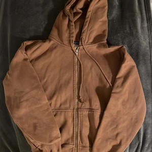 Brun hoodie med dragkedja - Säljer en brun hoodie i bomull med dragkedja framtill. Den har en skön huva med dragsko och långa ärmar med ribbade muddar. Perfekt för höst och vår när du vill ha något bekvämt och stilrent. Passar både till vardags och chillkvällar. 🧥