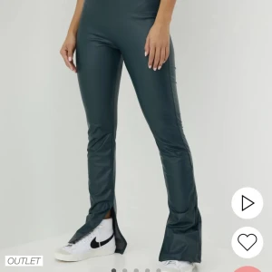 Mörkgröna skinnbyxor med slits från Nelly - Snygga mörkgröna byxor i syntetmaterial med hög midja och bootcut-stil. De har en cool slits vid bensluten som ger en extra touch. Perfekta för både vardag och fest! 🖤
